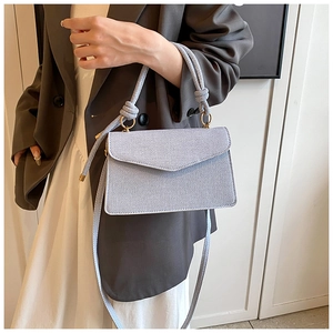 Detail of light blue crossbody bag with woven handle on a model in gray blazer