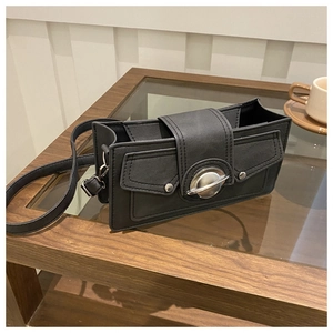 Detail of black faux leather shoulder bag featuring a silver circular buckle on a wood table