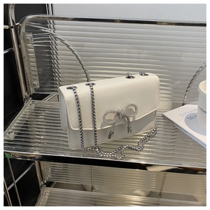 Detail of white leather crossbody bag with a sparkling rhinestone bow and silver chain strap