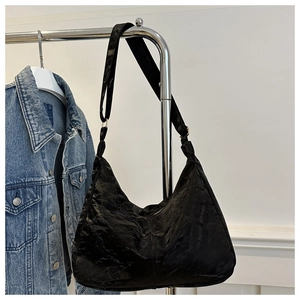 Detail of a black oversized tote bag featuring a waxed texture and adjustable shoulder strap