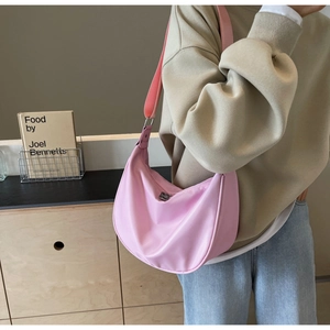 Detailed view of pink nylon crescent bag styled on shoulder with wide strap and zipper