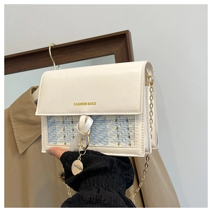 Detail of cream flap bag with blue tweed texture and gold chain strap and charm