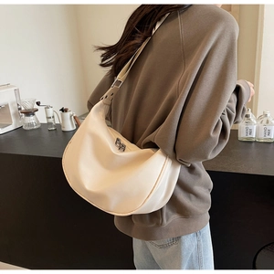 Detail view of a cream-colored leather crescent bag with adjustable wide strap on model
