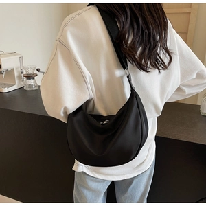 Detail of a minimalist black crescent nylon crossbody bag worn in a casual cafe setting