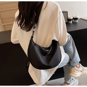 Minimalist black nylon crescent bag shown with wide shoulder strap in a lifestyle setting