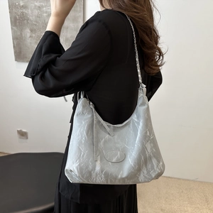 Silberne Hobo-Tasche mit Falten und Kettenriemen am Modell für einen trendigen Sommerlook