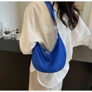 Detail of blue nylon crescent bag with silver dual zippers on adjustable strap