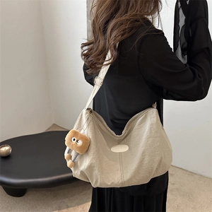 Chic beige nylon tote bag with a fun plush charm shown in a stylish crossbody position