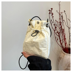 Close-up of minimalist off-white drawstring bucket bag with textured nylon and black cord