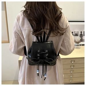 Détail d'un mini sac à dos noir avec lacets croisés et grand nœud décoratif à l'arrière
