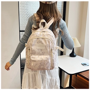 Detail of a beige backpack with bear prints and a front pocket on a model in a room