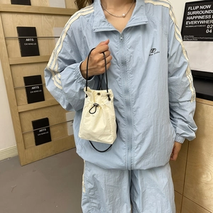 Minimalist cream drawstring bucket bag with black strap and sporty blue outfit