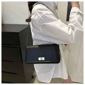 Dettaglio della borsa a tracolla nera con chiusura dorata su outfit camicia bianca