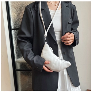 Close-up of a white pleated croissant bag with adjustable strap worn as a shoulder bag