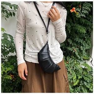 Outdoor shot of a black leather croissant bag with segmented stitching and crossbody strap