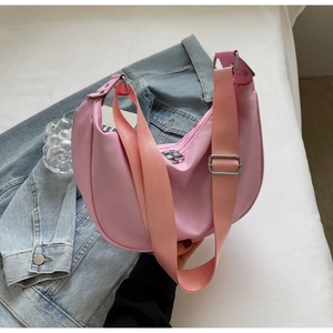 Pink nylon crescent shoulder bag with adjustable strap shown on a blue denim jacket