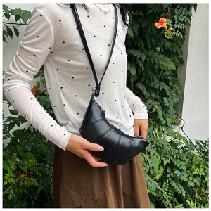 Detail of a black crescent crossbody bag with quilted segments worn in a garden setting