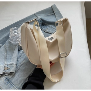 Close-up of off-white nylon crescent bag with wide strap and silver buckle on denim