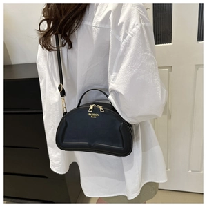 Detail of minimalist black half-moon bag featuring gold dual zippers and adjustable strap