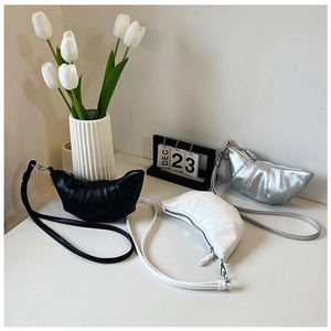 Three pleated croissant bags in black, white and silver on a minimalist display