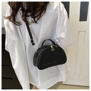 Detail of black crossbody bag with gold zipper and adjustable strap worn on white shirt