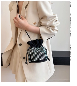 Detail of a black drawstring bucket bag with rhinestones worn by a model in a beige suit