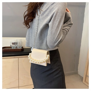 Detail view of a beige pearl chain flap crossbody bag worn by a model in a minimal setting
