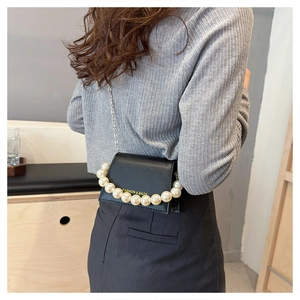 Detail of black mini crossbody bag with pearl handle and metal chain strap on model