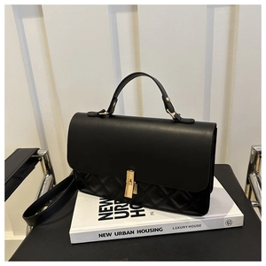 Detail of black quilted leather shoulder bag with gold rectangular clasp and top handle