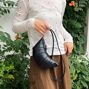 Chic black croissant shoulder bag with pleated details on a model in outdoor setting