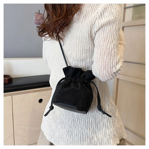 Detail of black rhinestone bucket bag with drawstring closure on model in knit sweater
