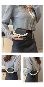 Detail of small black flap bag featuring pearl handle and silver chain strap