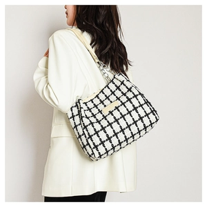 Detail of black and white plaid tweed tote bag with metal chain strap on white blazer
