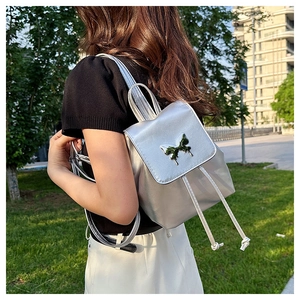 Close-up of metallic silver backpack featuring a decorative metal butterfly and drawstring