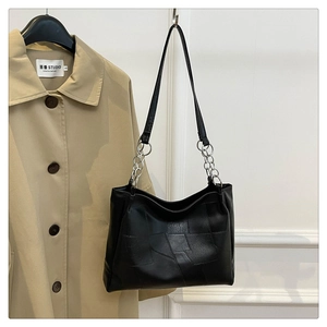Detail of black leather tote bag featuring a silver metal chain strap and geometric stitching