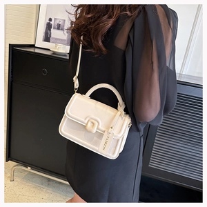 Detail of a chic cream-colored small square bag with a top handle and hanging fashion tag