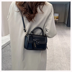 Detail of a black leather crossbody bag with a metal buckle and FASHION tag on a beige blazer