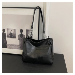 Detail of black tote bag featuring geometric square patchwork and silver chain strap accents