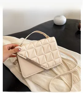 Detailed shot of beige quilted handbag with gold metal bar and top handle strap