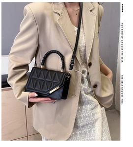 Detail of black quilted crossbody bag with triangle texture and woven handle on a beige suit