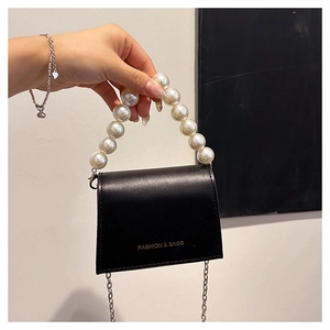Detail of black mini crossbody bag featuring white pearl handle and gold logo text