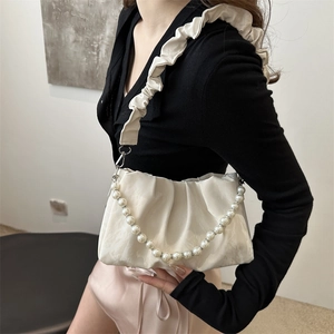 Elegant cream pleated cloud bag with pearl strap worn by a model in a minimalist setting