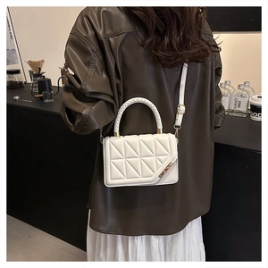 White quilted crossbody bag with gold metal trim and woven handle on person in brown jacket