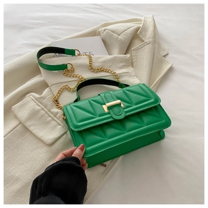 Detail of green quilted handbag showing gold chain strap and metal clasp on beige suit