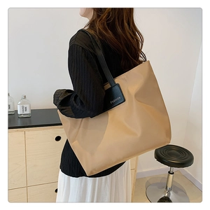 Detail of a large beige tote bag showing the black shoulder strap and fashion label detail