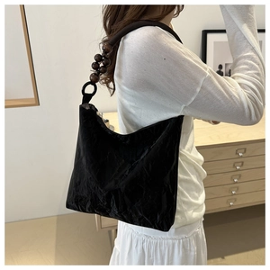 Close-up of black pleated tote bag featuring large dark brown wooden bead shoulder strap