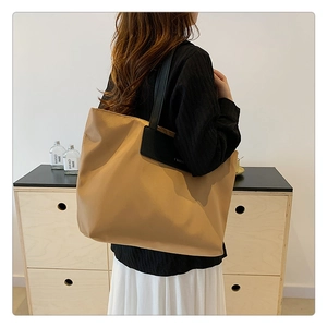 Close-up of khaki nylon tote bag with black leather straps worn by a model in interior
