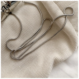 Close-up of a sleek silver metal snake chain on a textured beige corduroy surface