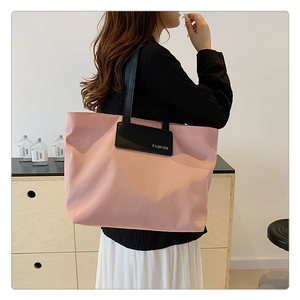 Detail showing the light pink nylon tote bag with black fashion label patch and handle