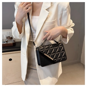 Detail of black quilted crossbody bag with rhombus pattern and metal trim on white suit